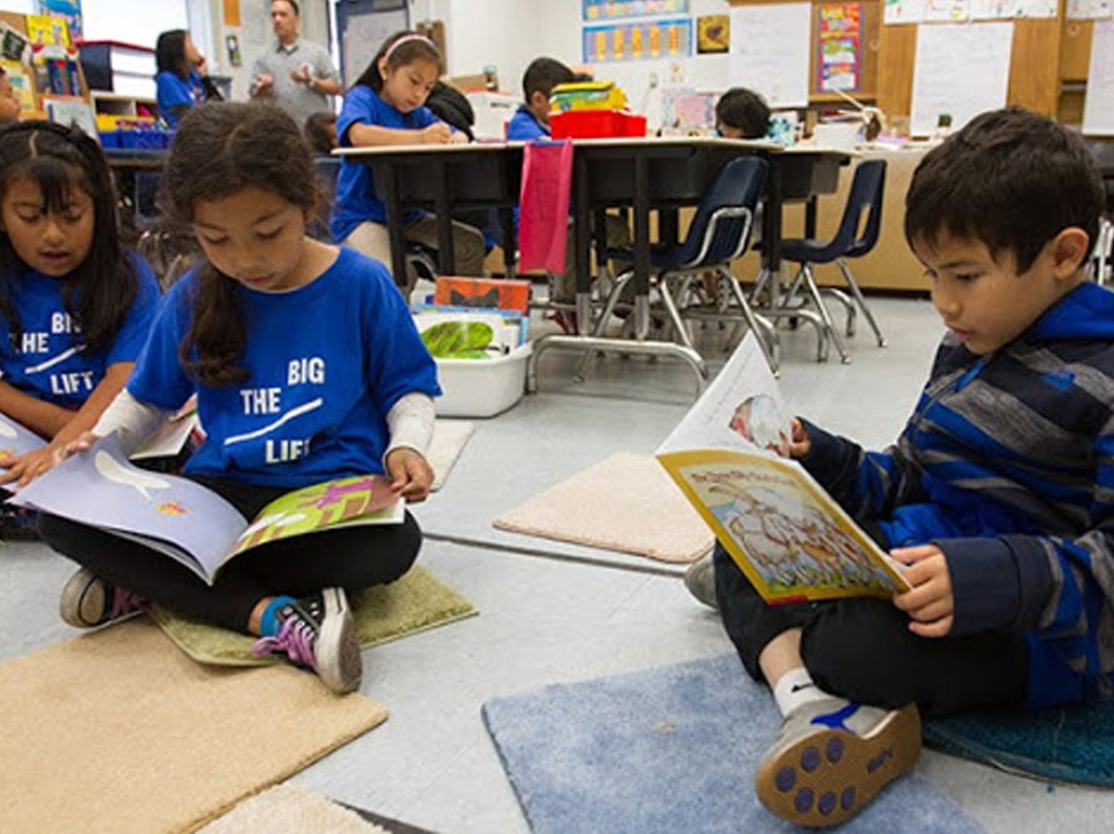 an image of children sitting cross-legged on the floor reading large children\'s books